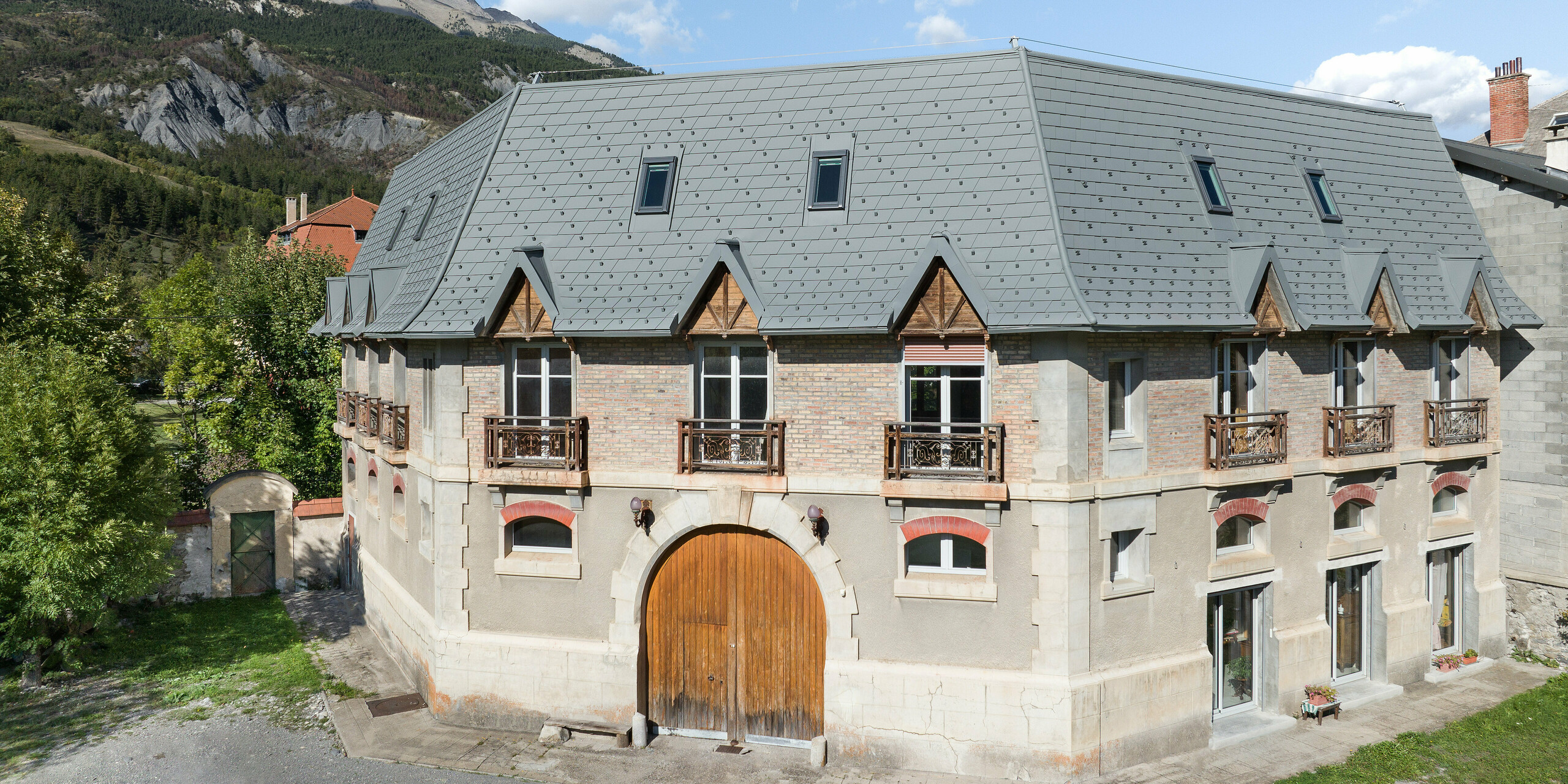 Pogled s sprednje strani na posestvo v kraju Barcelonnette v Franciji. Velika strešna površina je bila sanirana s strešnimi skodlami PREFA v P.10 svetlo sivi barvi. 