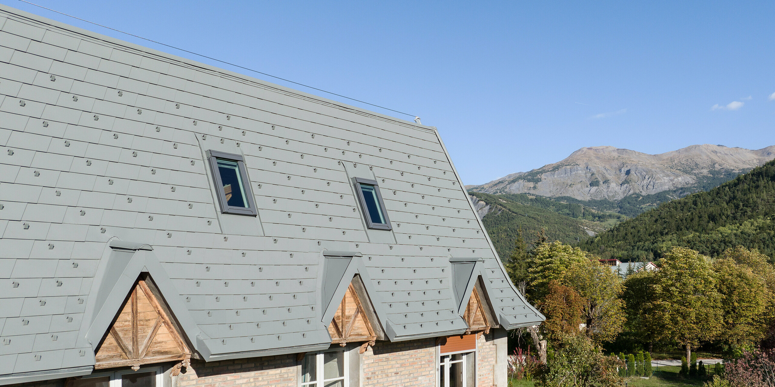 Velika strešna površina hiše na posestvu v kraju Barcelonnette v Franciji je bila obnovljena s strešnimi skodlami PREFA v P.10 svetlo sivi barvi.