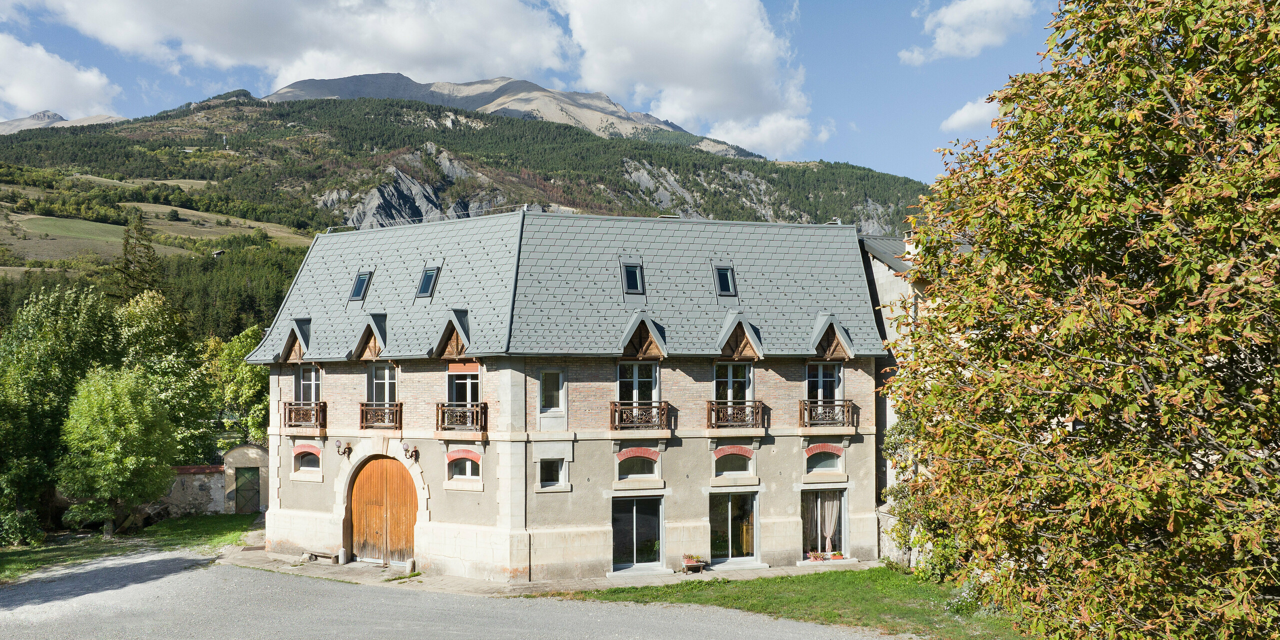 Pogled s sprednje strani na posestvo v kraju Barcelonnette v Franciji. Velika strešna površina je bila sanirana s strešnimi skodlami PREFA v P.10 svetlo sivi barvi. 