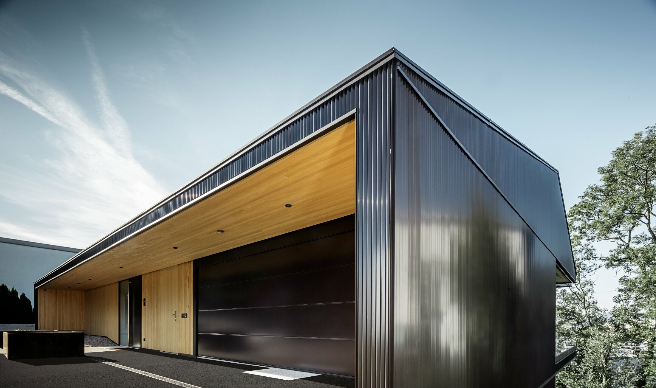 Garageneinfahrt eines Einfamilienhauses, die Fassade ist mit dem PREFA Zackenprofil in dunklem Braun verkleidet. 