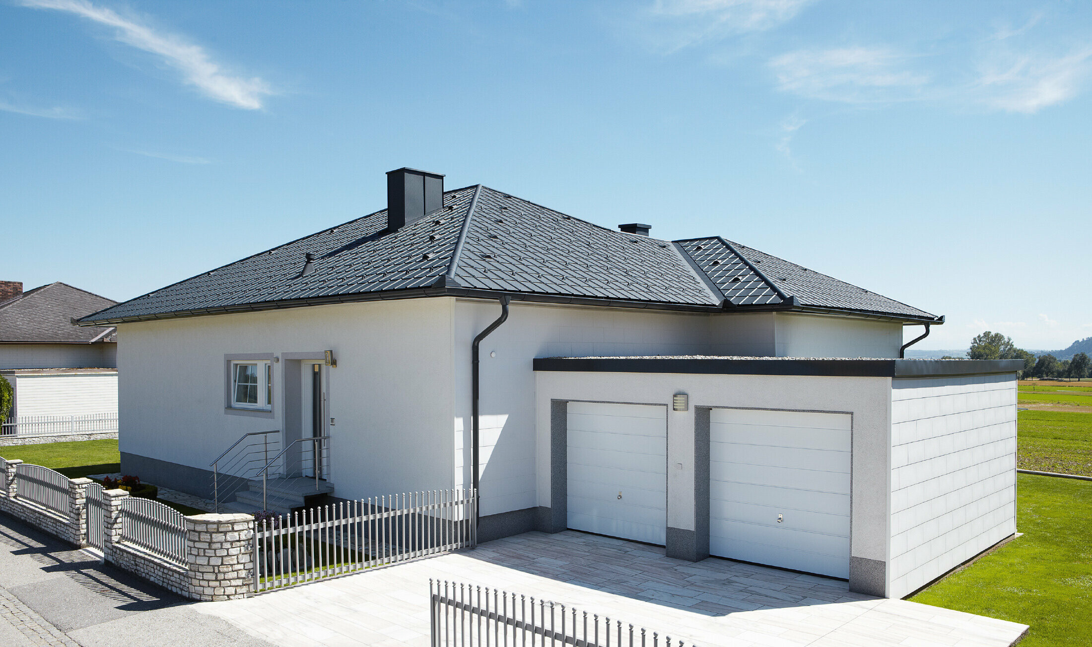 Der neugebaute Bungalow mit Zeltdach wurde mit der PREFA Dachplatte in P.10 Anthrazit eingedeckt. Rechts daneben wurde eine Doppelgarage angebaut, fotografiert wurde von der Straße aus.