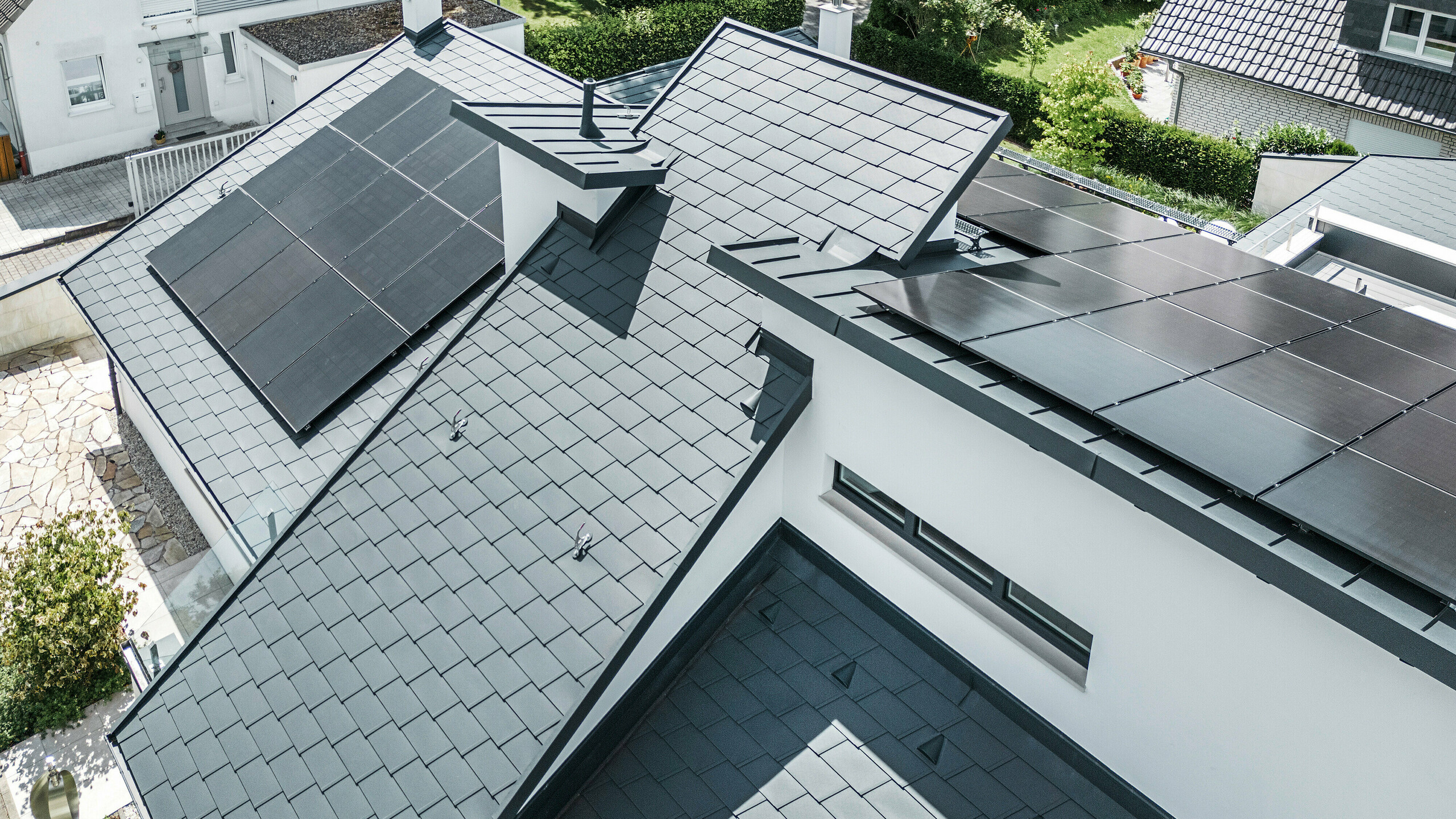 Pogled s ptičje perspektive na različne ravni strehe sodobne samostojne hiše v Dortmundu, ki je bila opremljena s strešniki PREFA DS.19 in PREFALZ v antracitni barvi P.10 ter z obsežnim fotovoltaičnim sistemom.