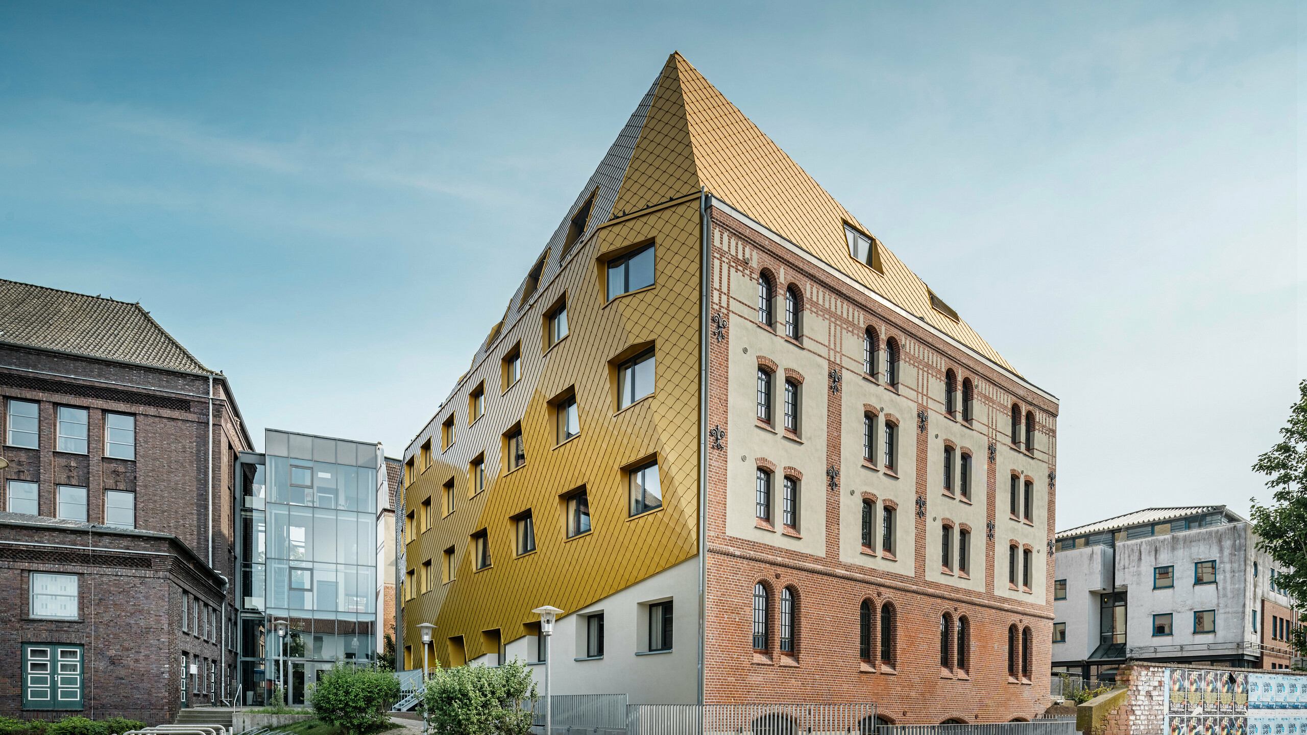 Talni posnetek postaje v Kielu. Študentski dom je viden diagonalno od strani. Na sliki je jasno viden izrazit kontrast med aluminijasto fasado iz PREFA strešnimi in fasadnimi rombi  29 × 29 v barvi Mayagold na levi ter spomeniško zaščiteno fasado iz ometa in opeke na desni.