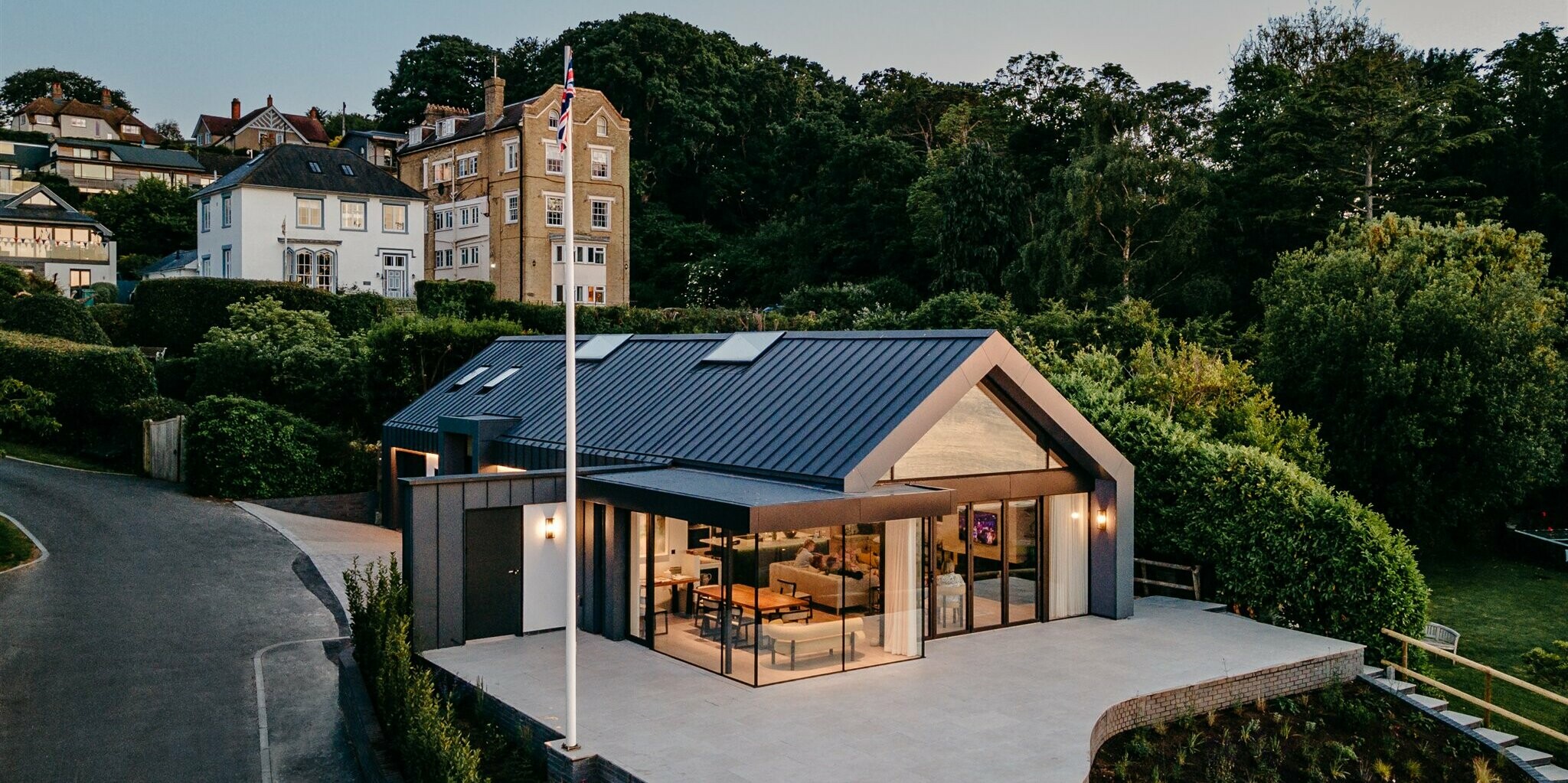 Dieser luxuriöse Bungalow auf der Isle of Wight kombiniert moderne Architektur mit atemberaubender Aussicht. Die dunkelgraue PREFALZ-Gebäudehülle verleiht dem Anwesen eine schlichte Eleganz und integriert es sanft in die üppige Landschaft. Durchdachte Verglasungen maximieren die malerischen Meerblicke und bewahren zugleich die Intimität. Das Haus ist ein perfektes Beispiel für zeitgenössisches Design, das die Schönheit seiner natürlichen Umgebung respektiert und hervorhebt.