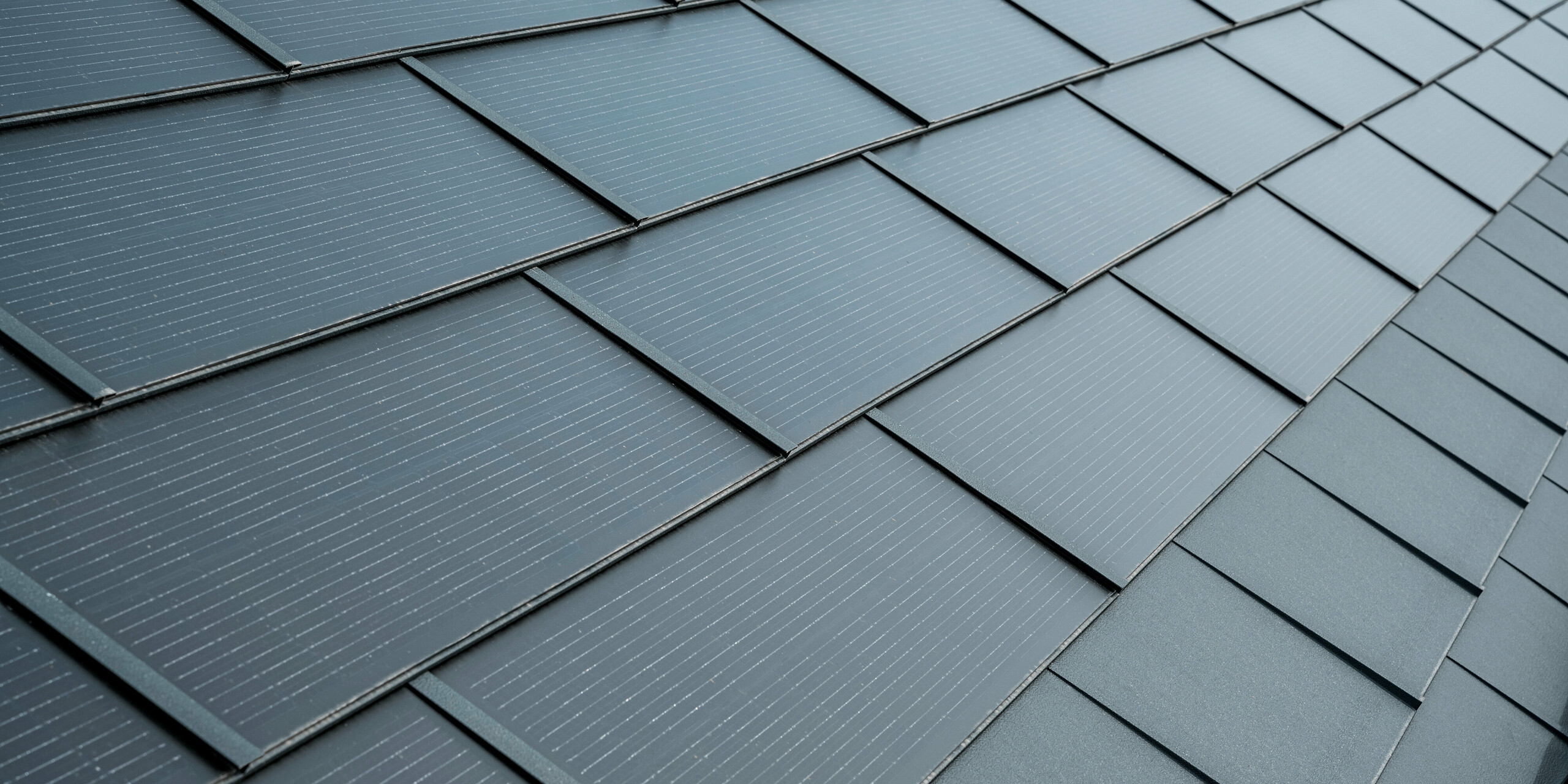 Bližnji posnetek strehe s PREFA solarnimi strešnimi ploščami v antracitni barvi. Solarni moduli so elegantno integrirani v streho in se harmonično prilegajo celotnemu videzu. Strešne plošče imajo teksturirano površino z drobnimi linijami, ki zagotavljajo dodatno estetiko, hkrati pa služijo kot funkcionalna in energetsko učinkovita rešitev.