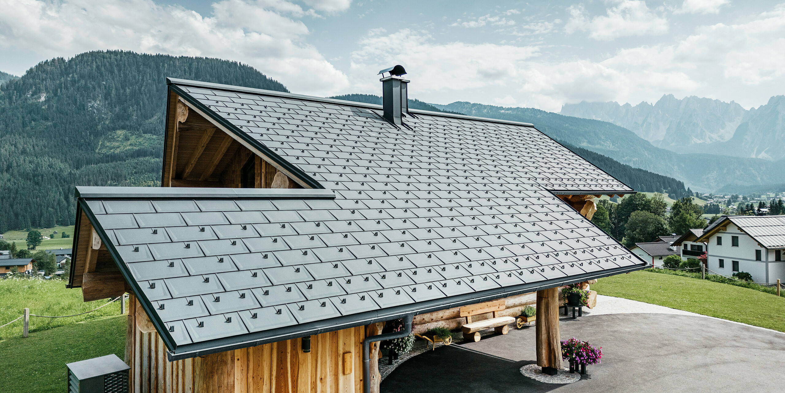 Moderna in hkrati tradicionalna arhitektura združeni v brunarici v kraju Gosau v Avstriji. Lesena hiša ima streho iz PREFA strešnih plošč R.16 v P.10 antracitni barvi. Pogled iz zraka prikazuje natančnost strešne konstrukcije, popolno integracijo v zasnovo brunarice in idilično vpetost v alpsko pokrajino z dih jemajočo gorsko panoramo v ozadju. Strešne plošče dajejo hiši sodoben pridih in so v skladu z okolju prijazno in trajnostno gradnjo.