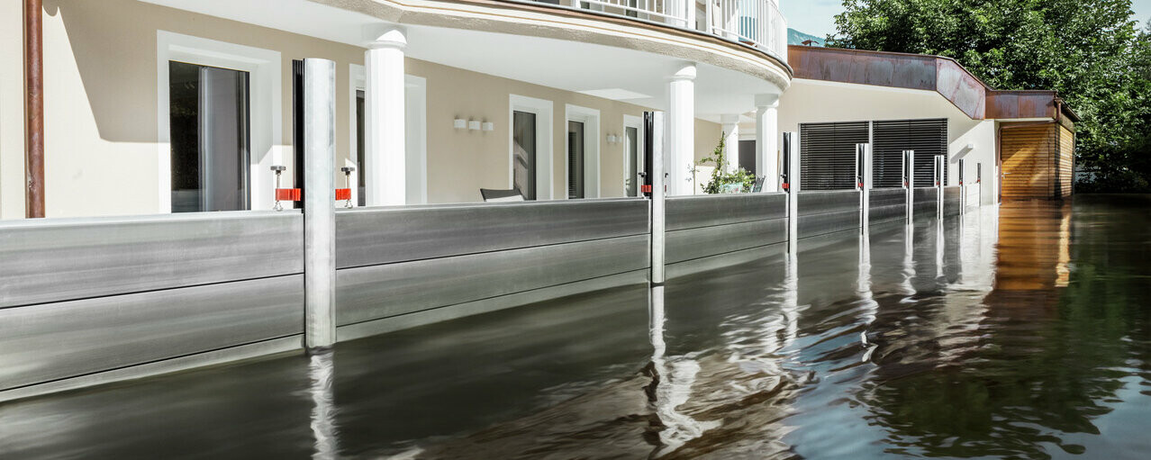 Na sliki je samostojna hiša z balkonom. Protipoplavni sistem PREFA varuje hišo pred že naraslimi poplavnimi vodami.