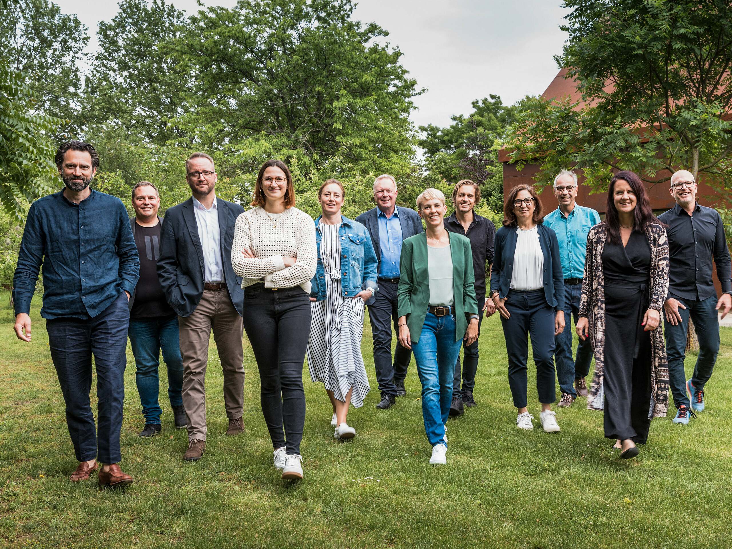 Gruppe von Expert:innen und Architekt:innen beim PREFARENZEN 2025 Dialog: Die Jury besteht aus zehn Architekt:innen und PREFA Expert:innen, die gemeinsam auf einer grünen Wiese vor der Residenz Velich im burgenländischen Seewinkel in eine gemeinsame Richtung gehen. Sie lächeln und gehen frontal auf die Kamera zu. Im Hintergrund ist die üppige Vegetation der Umgebung zu sehen. Das Bild entstand bevor die Jury die spannendsten Architekturobjekte für die PREFA Architekturplattform 2025 auswählte. Beim PREFARENZEN Dialog im Mai 2024 lag der Fokus auf der Funktionalität und Einfachheit sowie dem Mehrwert moderner Architekturobjekte. Auf dem Bild zu sehen v. l. n. r.: Thomas Heil (Co-Gründer, dreiplus Architekten), Jürgen Haller (Baumeister, Jürgen Haller GmbH), Christian Wirth (Leiter Objektberatung, PREFA Österreich), Chiara Desbordes (Head of Content, Architektur Aktuell), Paulina Frey (Marketingleiterin, PREFA Schweiz), Gerald Krebs (Objektberater, PREFA Österreich), Veronika Roll (Marketing PREFA Österreich), Daniel Luckeneder (Associate Partner, laac zt gmbh), Patricia Ezcurra (Architektin, wwa Architekten), Wolfgang Croce (Croce & Wir, Graz), Bettina Almeida (Kommunikationsmanagement, PREFA), Jürgen Jungmair (Marketingleiter International, PREFA).